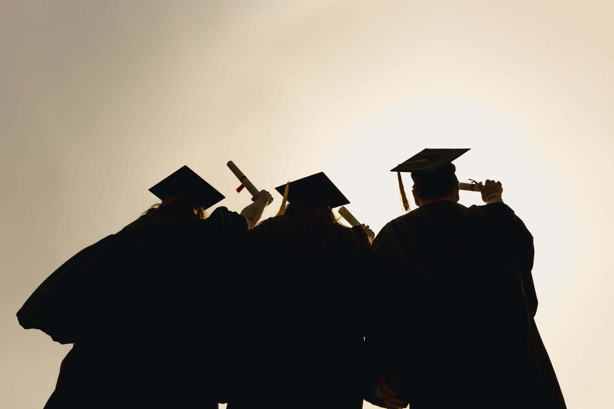 How to Make Graduation Invitations - Graduates celebrating with diplomas at sunset.