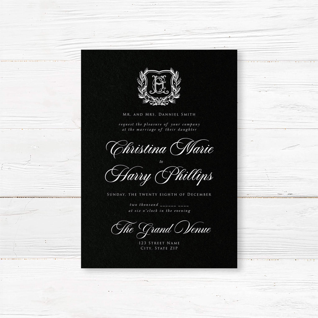 Elegant wedding invitation with black background, vintage-style white shield monogram surrounded by a laurel wreath, white calligraphy and serif fonts, ideal for formal or gothic weddings.