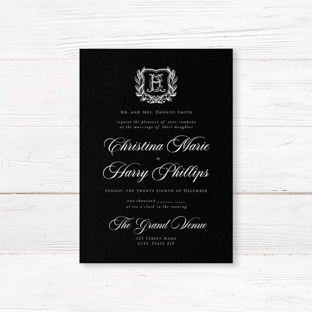 Elegant wedding invitation with black background, vintage-style white shield monogram surrounded by a laurel wreath, white calligraphy and serif fonts, ideal for formal or gothic weddings.