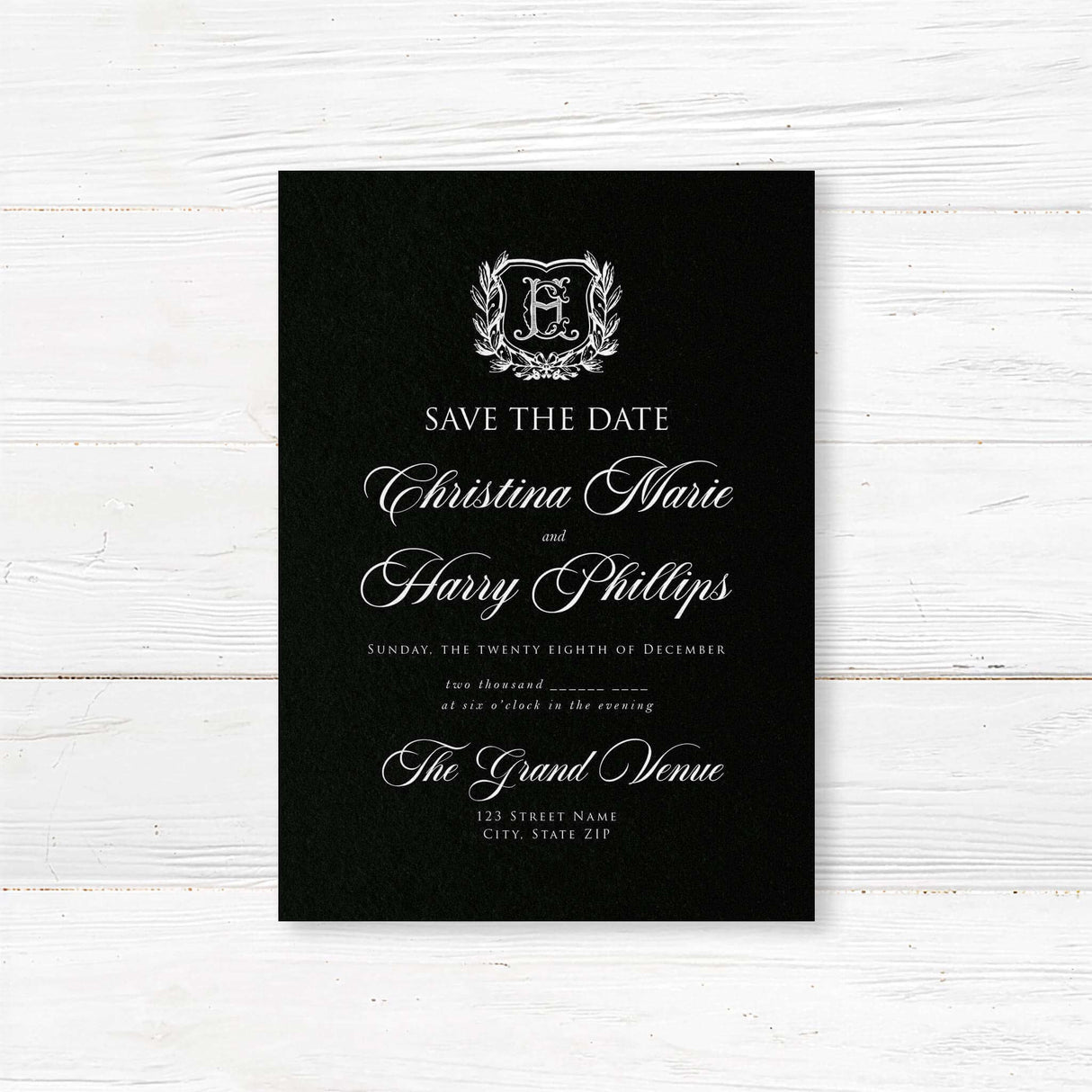 Save the Date card with black background, vintage-style shield crest encircled by a laurel wreath, and elegant white calligraphy and serif fonts for formal weddings.