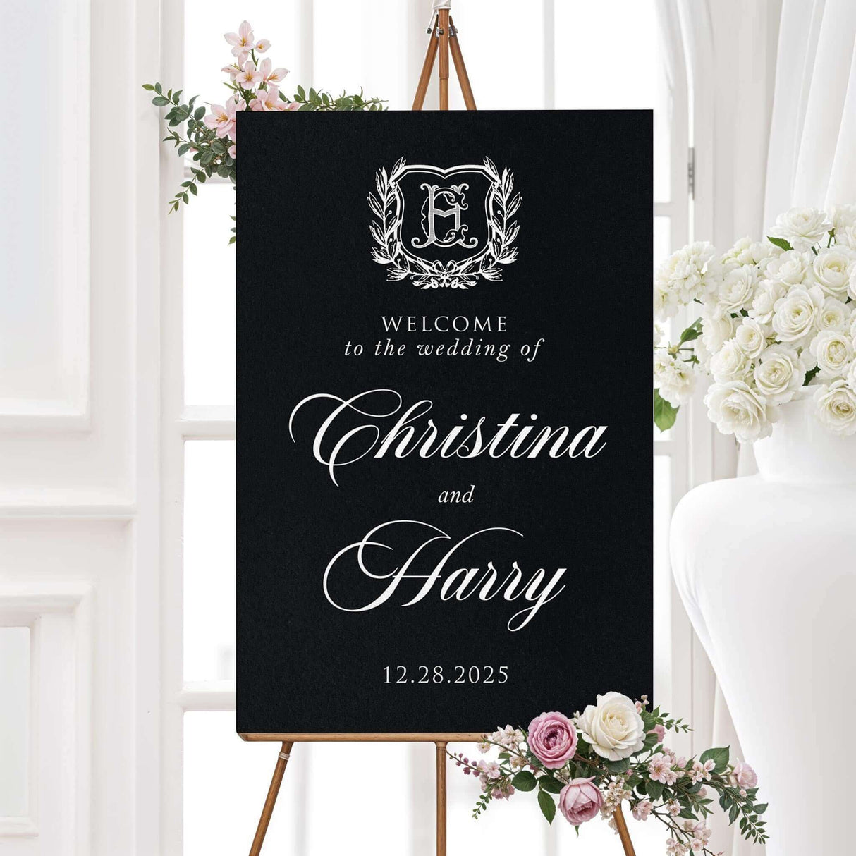 Wedding welcome sign with dramatic black background, vintage-style white monogram shield crest surrounded by a laurel wreath, and elegant white script and serif fonts.