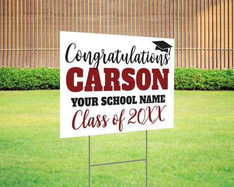 Custom graduation yard sign with bold name design in maroon and black, featuring a congratulatory message, a graduation cap graphic, and customizable school name and class year. Printed on durable Coreplast plastic, available in single or double-sided options. Perfect for high school and college graduates.