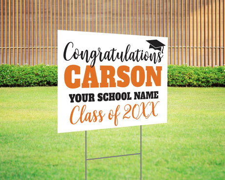 Custom graduation yard sign with bold name design in orange and black, featuring a congratulatory message, a graduation cap graphic, and customizable school name and class year. Printed on durable Coreplast plastic, available in single or double-sided options. Perfect for high school and college graduates.