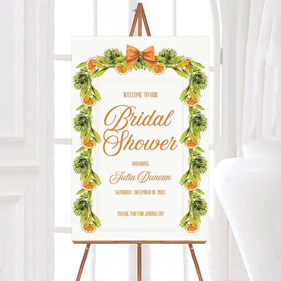Christmas Citrus Garland bridal shower welcome sign featuring watercolor evergreen greenery, dried orange slices, and an orange bow. This personalized holiday bridal shower sign displays customizable event details in elegant orange script.