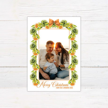 Personalized Christmas citrus garland family photo card featuring watercolor evergreen garlands, orange slices, and decorative orange bows surrounding a customizable family photograph. The coordinating back features a horizontal citrus greenery garland on a white background.