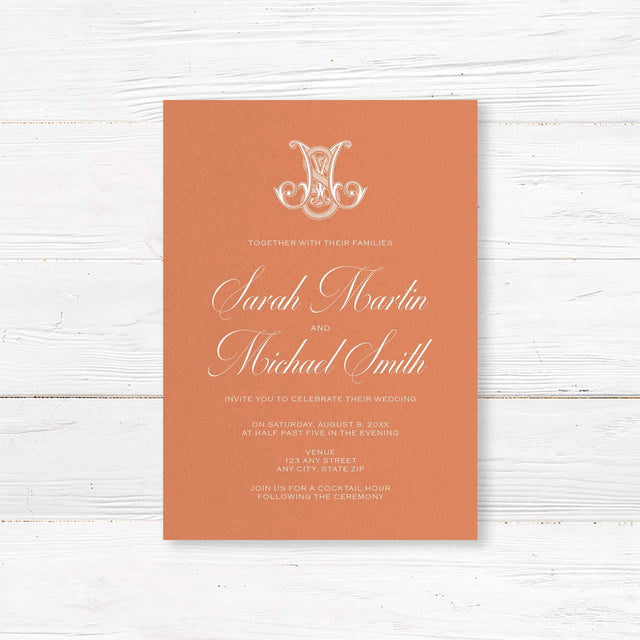 Terracotta wedding invitation with white calligraphy and ornate Celtic-style monogram