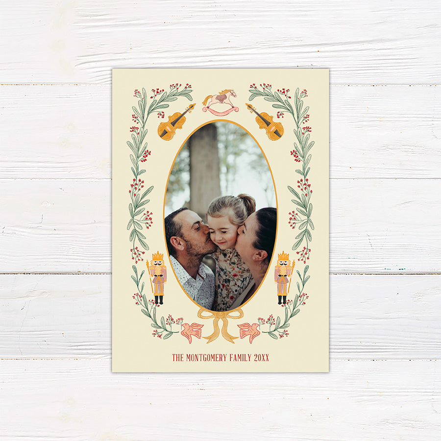 Personalized Christmas photo card featuring an oval family photo surrounded by nutcrackers, greenery, berries, bows, and musical instruments.