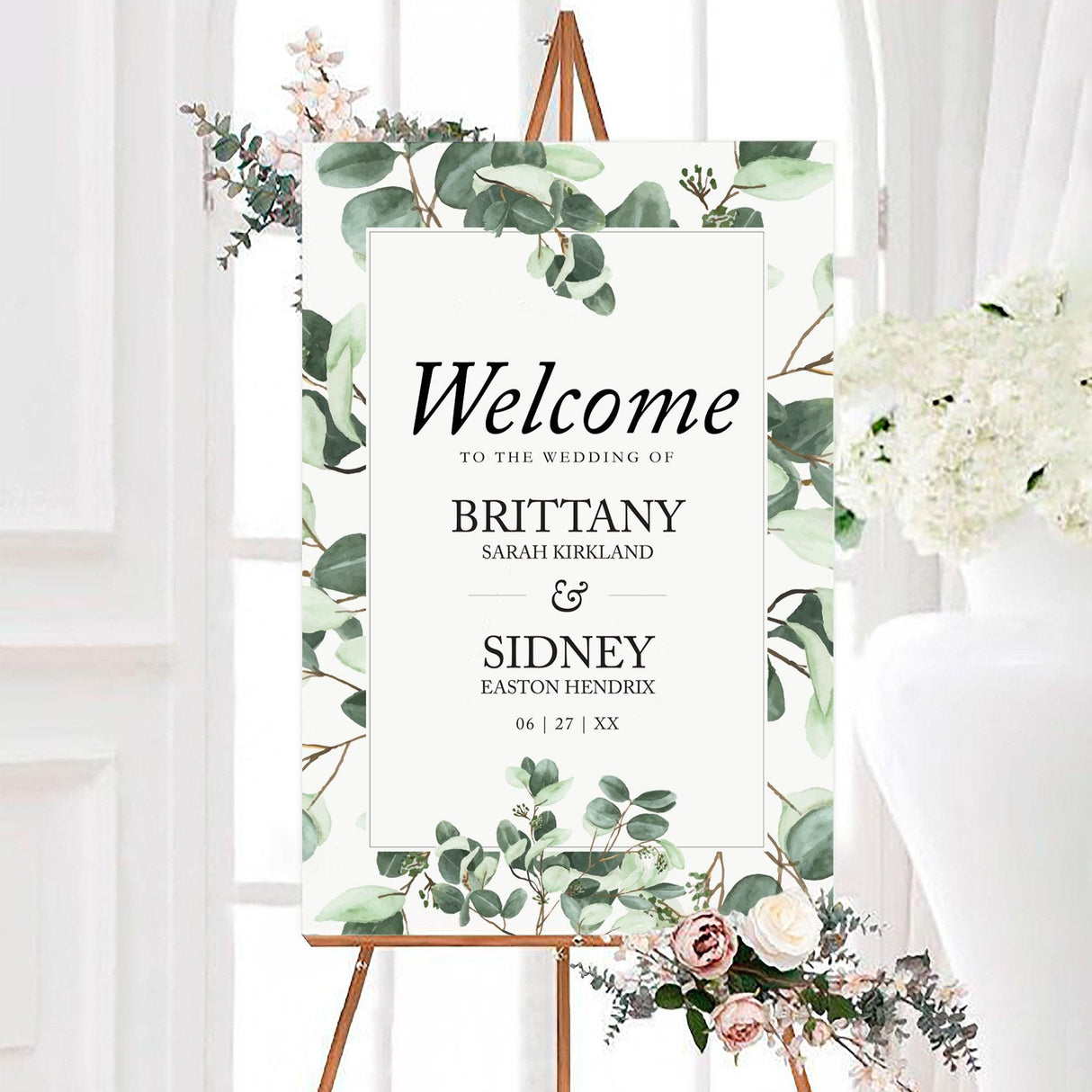 A wedding welcome sign with a white background features a lush greenery design of watercolor eucalyptus leaves framing the layout. The text is centered within a clean, black-bordered rectangle, using a mix of serif and script fonts for an elegant and modern touch. The word "Welcome" is prominently displayed at the top, followed by details of the wedding date. This design exudes natural simplicity and sophistication, making it perfect for a botanical, minimalist, or rustic wedding celebration.