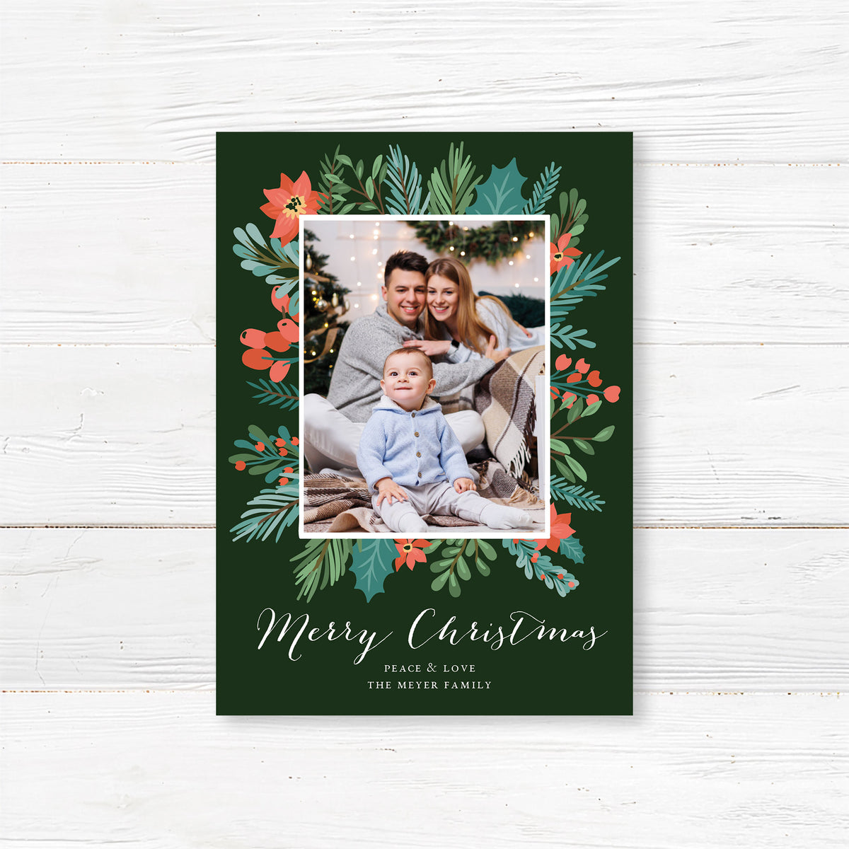 Personalized festive garland frame photo Christmas card featuring a family photograph framed by festive greenery, poinsettias, holly, and berries with elegant Merry Christmas lettering. The coordinating back features a repeating Christmas botanical pattern on a deep green background.
