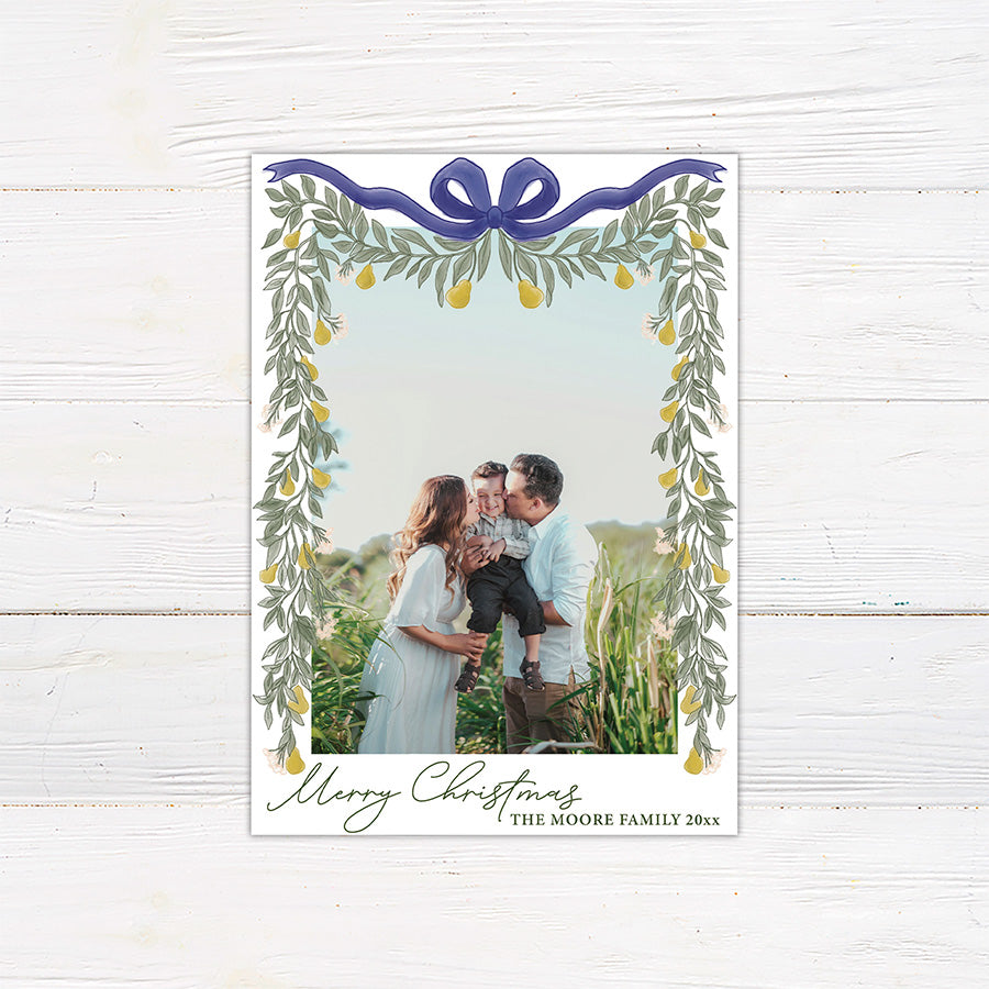 Personalized Christmas photo card featuring a family picture framed by cascading greenery, golden pears, and an elegant ribbon bow. The design includes a Merry Christmas greeting with a custom family name and year.