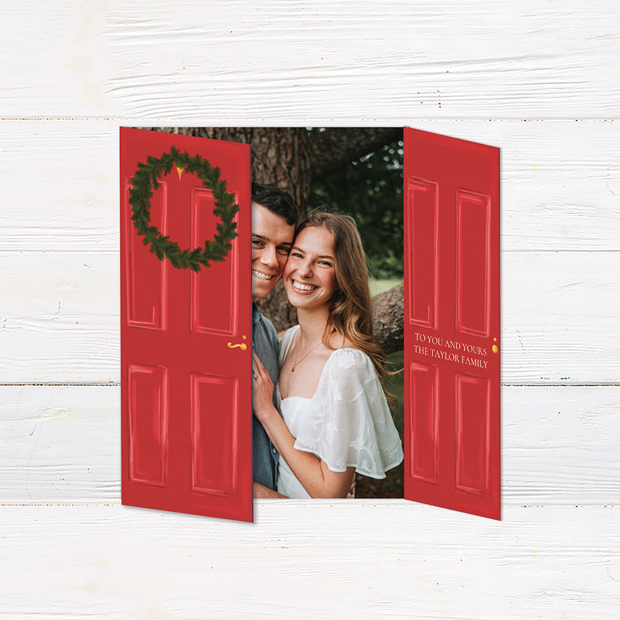 Personalized Home for the Holidays Christmas gatefold photo card featuring festive red double doors decorated with evergreen wreaths and customizable family photos. The folding holiday card opens to reveal a large photo and personalized Christmas greeting with an additional four-photo collage. Four-photo variant.
