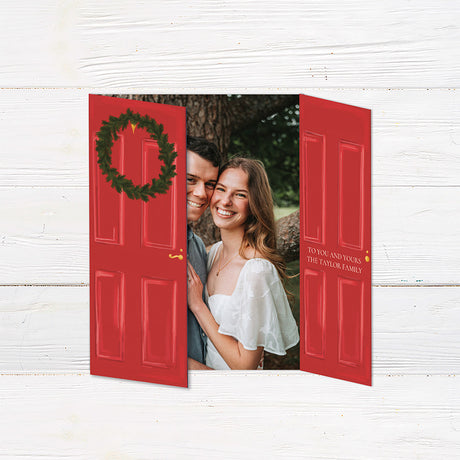 Personalized Home for the Holidays Christmas gatefold photo card featuring festive red double doors decorated with evergreen wreaths and customizable family photos. The folding holiday card opens to reveal a large photo and personalized Christmas greeting with an additional four-photo collage. Four-photo variant.