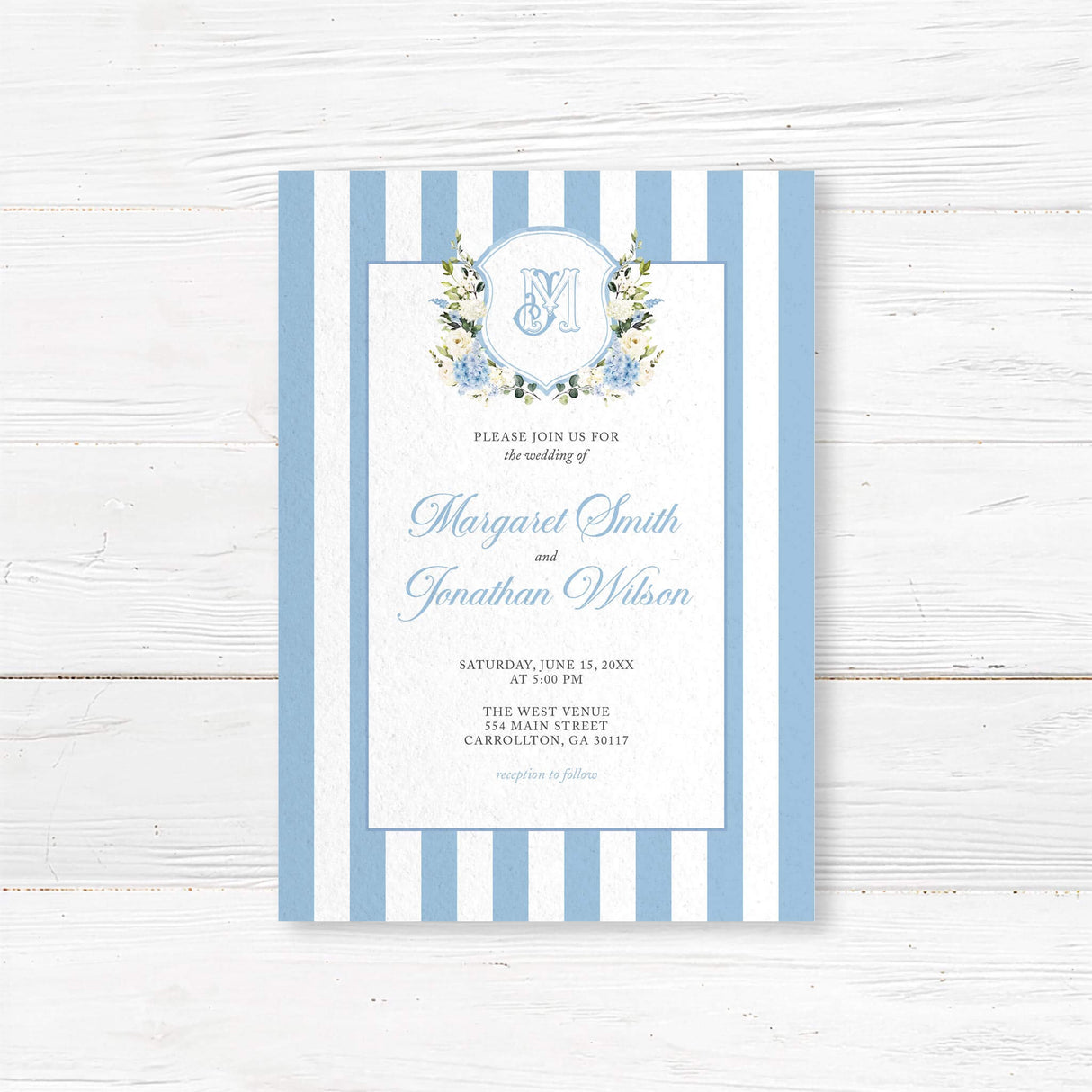 Wedding invitation with powder blue and white vertical stripes, floral monogram crest of blue hydrangeas and white roses, and elegant script and serif fonts on a white center panel, ideal for spring weddings.