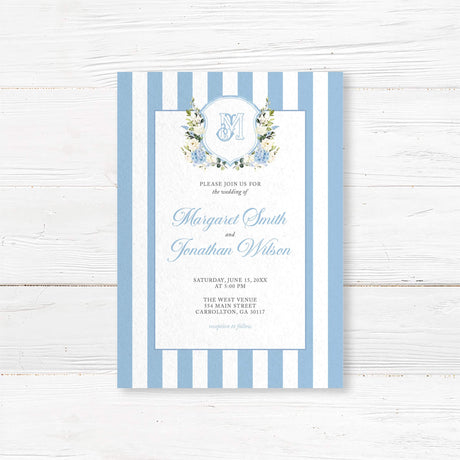 Wedding invitation with powder blue and white vertical stripes, floral monogram crest of blue hydrangeas and white roses, and elegant script and serif fonts on a white center panel, ideal for spring weddings.