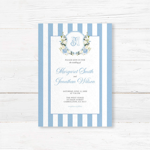 Wedding invitation with powder blue and white vertical stripes, floral monogram crest of blue hydrangeas and white roses, and elegant script and serif fonts on a white center panel, ideal for spring weddings.