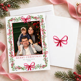 Personalized Christmas photo card featuring a family portrait framed by watercolor mistletoe, greenery, berries, and ribbon bows. The back features a coordinating watercolor bow.