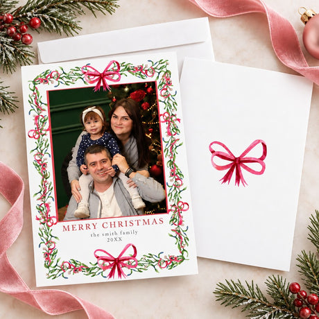 Personalized Christmas photo card featuring a family portrait framed by watercolor mistletoe, greenery, berries, and ribbon bows. The back features a coordinating watercolor bow.