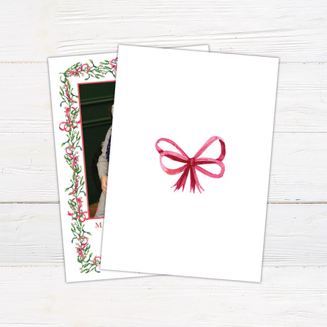 Personalized Christmas photo card featuring a family portrait framed by watercolor mistletoe, greenery, berries, and ribbon bows. The back features a coordinating watercolor bow.