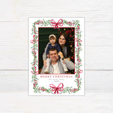 Personalized Christmas photo card featuring a family portrait framed by watercolor mistletoe, greenery, berries, and ribbon bows. The back features a coordinating watercolor bow.