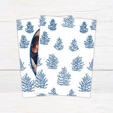 Personalized family Christmas photo card featuring an oval portrait surrounded by hand-drawn evergreen pine trees. A ribbon banner displays a Merry Christmas greeting and custom family name. blue