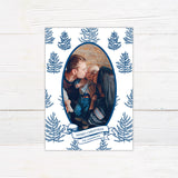 Personalized family Christmas photo card featuring an oval portrait surrounded by hand-drawn evergreen pine trees. A ribbon banner displays a Merry Christmas greeting and custom family name. blue