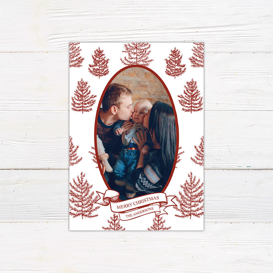 Personalized Winter Pine family Christmas photo card featuring an oval portrait surrounded by hand-drawn evergreen pine trees. A ribbon banner displays a Merry Christmas greeting and custom family name. red
