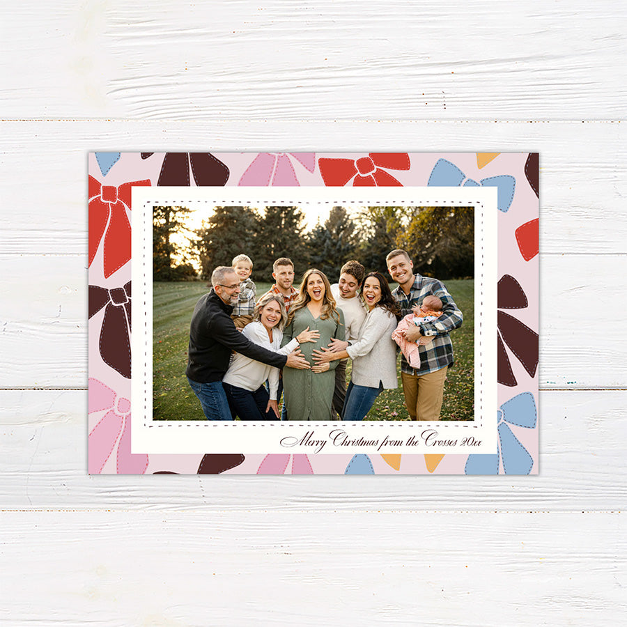 Personalized family Christmas photo card featuring a large photograph surrounded by a playful pattern of colorful ribbon bows. The coordinating back features an all-over illustrated bow pattern.