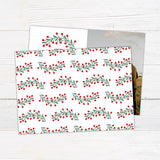 Personalized Our First Christmas photo card featuring a newlywed couple with festive greenery and red berries. The back features a coordinating botanical holiday pattern.