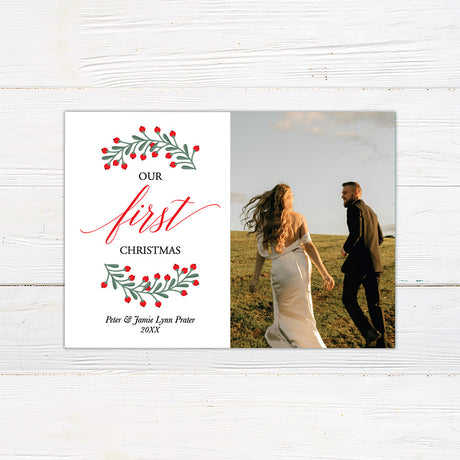 Personalized Our First Christmas photo card featuring a newlywed couple with festive greenery and red berries. The back features a coordinating botanical holiday pattern.