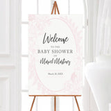A pink floral baby shower welcome sign with a soft pink floral oval frame on a white background. The design features delicate flowers and clean typography.