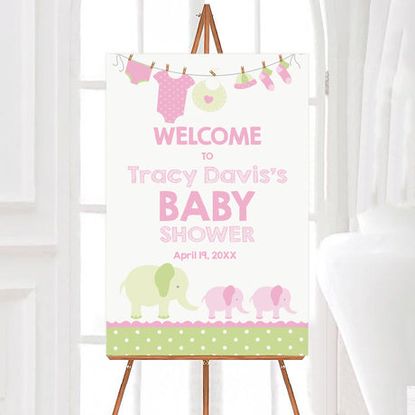 A pink green elephants baby shower welcome sign with pink and green elephants and baby clothes on a clothesline. The design uses soft pastel colors and playful illustrations.