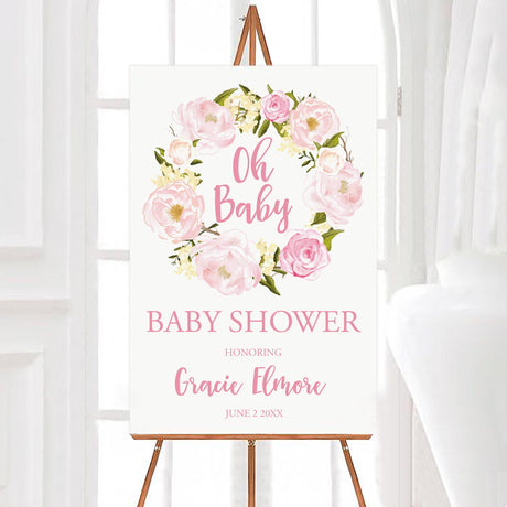 A pink wreath baby shower welcome sign with a pink floral wreath and soft blush lettering. The design features flowers arranged in a circular frame on a white background.