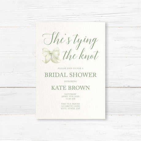 Watercolor bow bridal shower invitation that reads "She’s Tying the Knot" with floral accents,