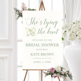 Watercolor bow bridal shower welcome sign that reads "She’s Tying the Knot" with floral accents,