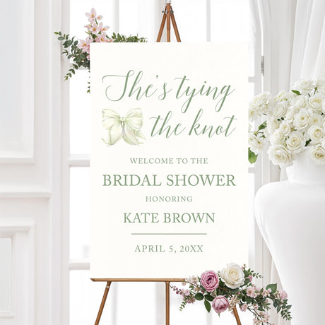 Watercolor bow bridal shower welcome sign that reads "She’s Tying the Knot" with floral accents,