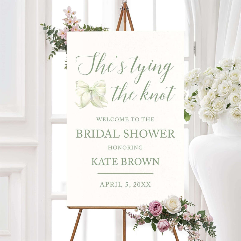 Watercolor bow bridal shower welcome sign that reads "She’s Tying the Knot" with floral accents,