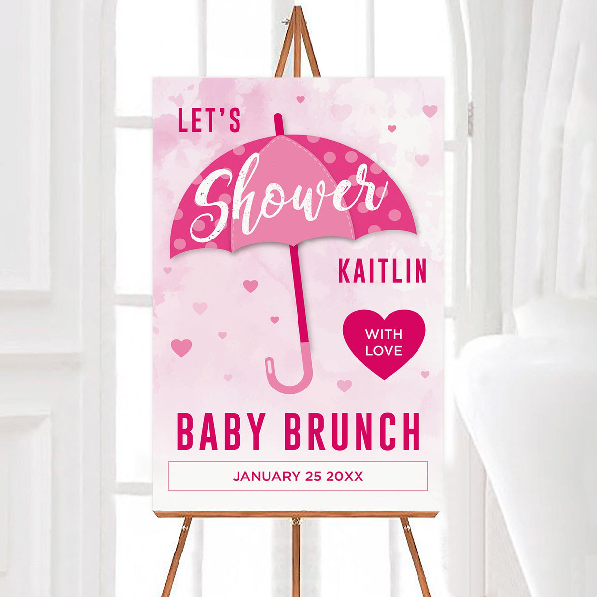 A shower with love pink baby shower welcome sign with an umbrella and heart accents. The design uses a soft watercolor background.