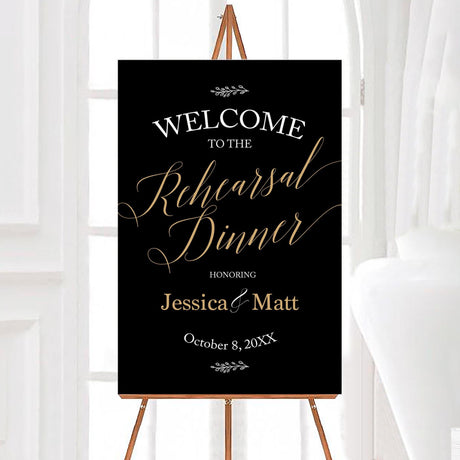 Elegant black and gold rehearsal dinner sign featuring the words "Welcome to the Rehearsal Dinner" in a stylish script font. The couple's names are displayed in a sophisticated serif font with a beautiful ampersand. The event date is elegantly placed at the bottom, with delicate leaf accents at the top and bottom of the sign for a chic, modern touch. Perfect for adding a classy and personalized welcome to your rehearsal dinner event.