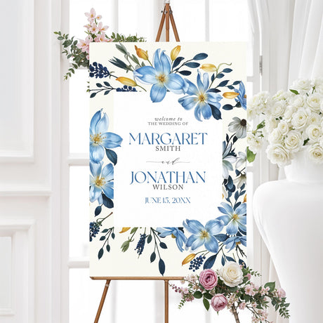 A sign with a soft cream background features an elegant floral border of blue, white, and yellow flowers with lush greenery. The text is centered within a white rectangle, using a mix of serif and script fonts for a sophisticated and timeless look. Event details, including the date, time, and venue, are clearly displayed. The design combines classic elegance with a modern floral touch.