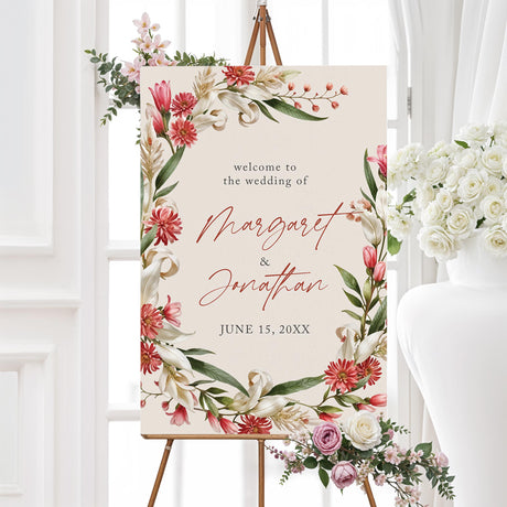 Elegant welcome sign with a floral design featuring red, pink, and white flowers with green leaves arranged in a wreath. The text is in a mix of script and serif fonts. 