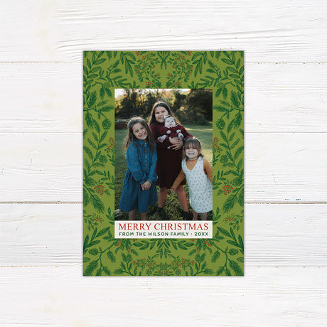 Personalized family Christmas photo card featuring winter greenery, berries, pinecones, and a large family portrait. The coordinating back includes three additional family photos surrounded by botanical holiday artwork.